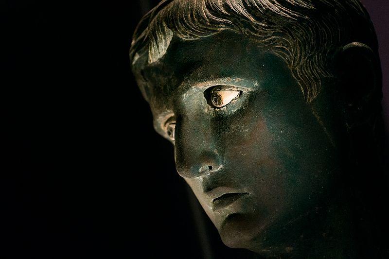 Side view of bronze statue head, against a black background