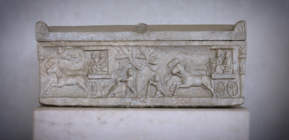 Small marble sarcophagus, with a relief depicting two horse drawn carts, a boy playing with a bird and an child with a walker.